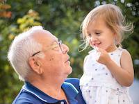 An elderly man holds his granddaughter in the air